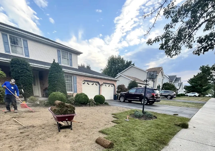 A crew member works beside a wheelbarrow as new sod is laid across a prepared front yard.